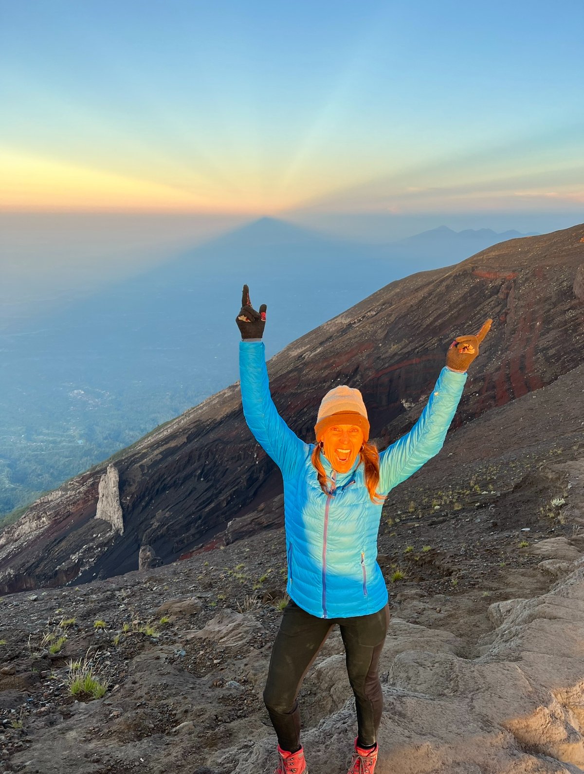 Jen at the mountain summit with arms raised in celebration